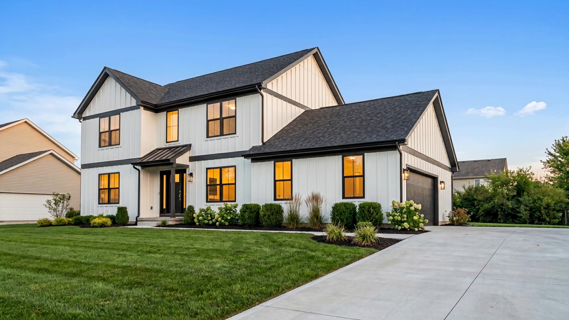Fully remodeled modern farmhouse at dusk with warm interior lighting and fresh landscaping